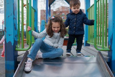 Erkek ve kız kardeşler sonbaharda oyun alanında eğlenirler.
