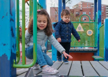 Erkek ve kız kardeşler sonbaharda oyun alanında eğlenirler.