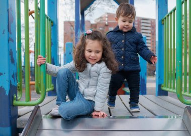 Erkek ve kız kardeşler sonbaharda oyun alanında eğlenirler.