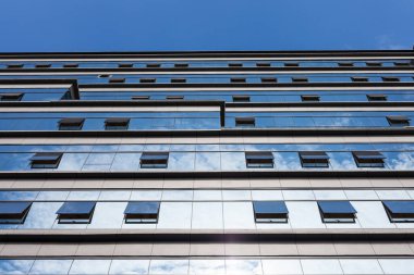 Bulutlu gökyüzünün altında tonlu cam ve çelikten yapılmış mavi perde duvarı.