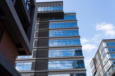 Bulutlu gökyüzünün altında tonlu cam ve çelikten yapılmış mavi perde duvarı.