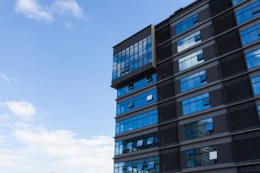 Bulutlu gökyüzünün altında tonlu cam ve çelikten yapılmış mavi perde duvarı.