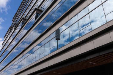 Bulutlu gökyüzünün altında tonlu cam ve çelikten yapılmış mavi perde duvarı.