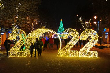 Khmelnytskyi, Ukrayna - 7 Aralık 2021: 2022 noel sokak dekorasyonunda insanlar ışık kemerlerinde yürüyorlar. Khmelnytskyi Noel sokak dekorasyonları.