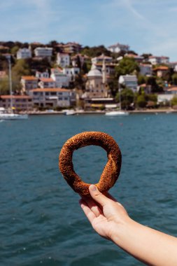 Deniz kenarında Türk usulü susamlı simit tutan bir kadın görüntüsü. 