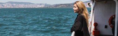 Siyah kazaklı bir kadının İstanbul 'da boğazdan geçen feribot teknesinden denize bakışının yan görüntüsü.