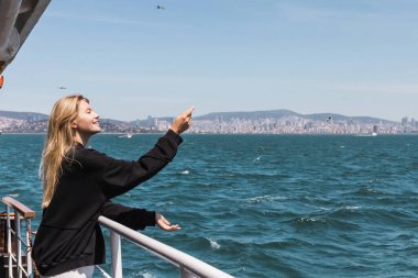 Siyah kazaklı mutlu kadın feribottan boğazı geçen denize bakıyor.