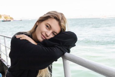 blonde young woman in black sweater looking at camera from ferry boat crossing bosphorus strait clipart