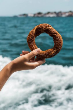 Boğazın yanında Türk usulü susamlı simit tutan genç bir kadın görüntüsü.