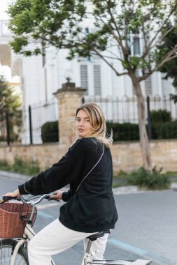 Bisiklete binen ve hindiyle caddede kameraya bakan şık giysili genç sarışın kadın.