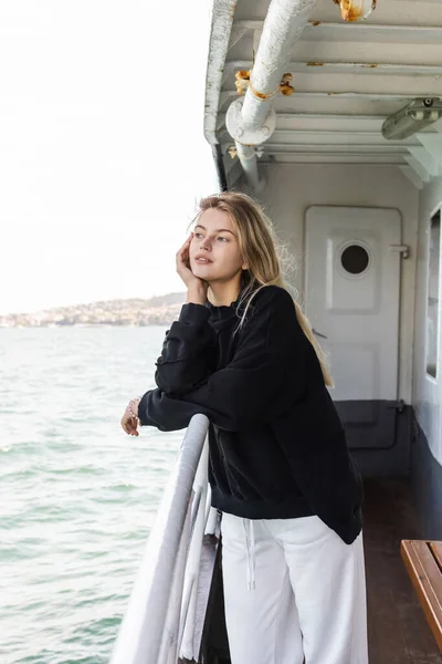 Rêveuse jeune femme en pull noir regardant la mer depuis le ferry traversant le bosphore à Istanbul — Photo de stock