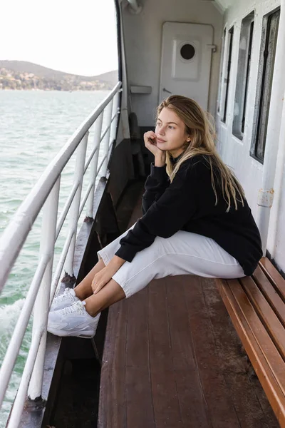 Donna sognante in maglione nero seduta sulla panchina guardando il mare dal traghetto che attraversa lo stretto di bosphorus — Foto stock