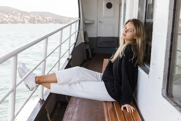 Rubia mujer en suéter negro sentado en el banco en ferry barco cruzar bosporus en istanbul - foto de stock