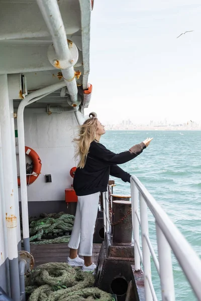 Vista lateral da mulher sorridente em camisola preta olhando para gaivota de barco de balsa cruzando bosporus em istanbul — Fotografia de Stock