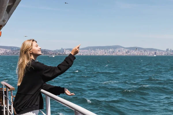 Happy woman in black sweater gesturing and looking at sea from ferry boat crossing bosphorus strait — Stock Photo