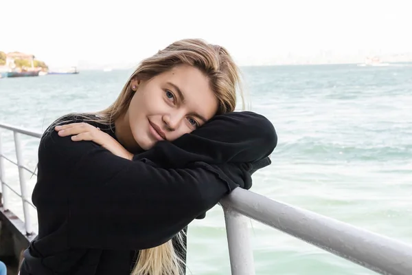 Bionda giovane donna in maglione nero guardando la fotocamera dal traghetto che attraversa lo stretto di bosphorus — Foto stock