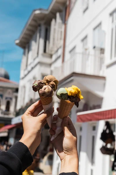 Vista ritagliata della donna che tiene gustosi coni gelato in mano sulla strada urbana — Foto stock