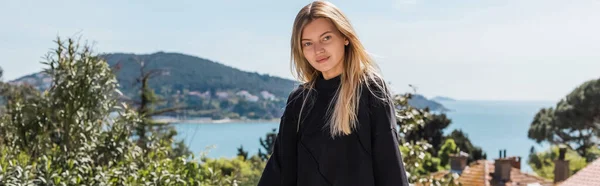 Junge blonde Frau posiert in der Nähe von Häusern und Meer auf Prinzessinneninseln in der Türkei, Banner — Stockfoto