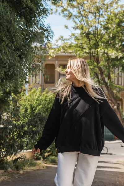 Young blonde woman in trendy outfit smiling while walking on street in turkey — Stock Photo