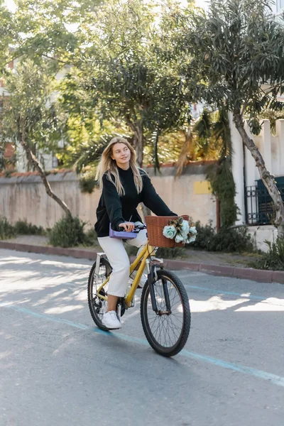 Молодая счастливая женщина в модном наряде катается на велосипеде по солнечной улице в индейке — стоковое фото