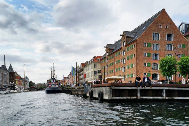 COPENHAGEN, NYHAVN - CIRCA HAVN Temmuz 2022: Kopenhag 'ın merkezindeki kanal ve cadde, Kongens Nytorv ve marina arasında yer almaktadır. Tarihi apartmanların, Danimarka bayraklarının, teknelerin ve turistlerin görünür renkli cepheleri.                            