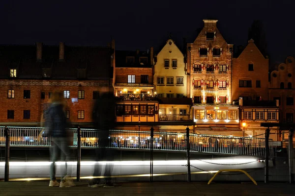 GDANSK, POLAND - CIRCA APRIL 2022: Motlawa Nehri üzerindeki yaya köprüsünün açılışını akşam saatlerinde bekleyen iki turist var. Arka planda, tarihi apartmanların görünen yüzleri var..