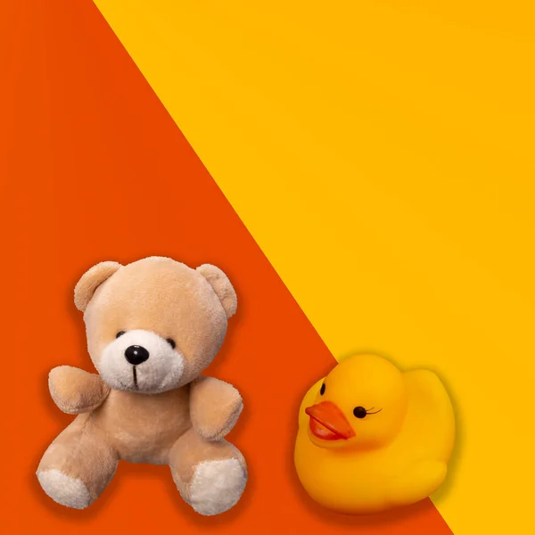Sarı ve turuncu arka planda plastik ördek ve oyuncak ayı..