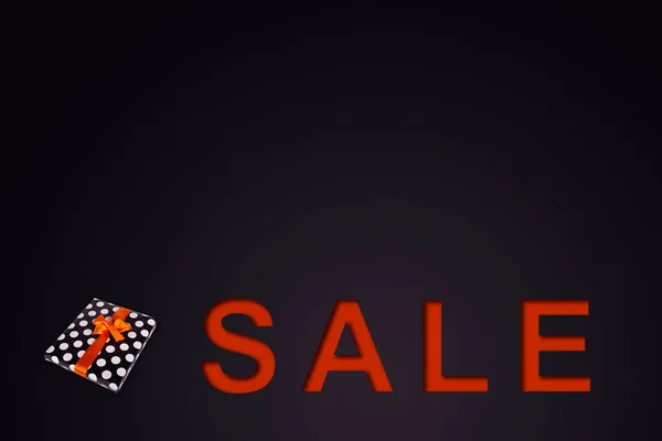 Satış afişi. Siyah arka planda turuncu kurdeleli bir hediye kutusu..