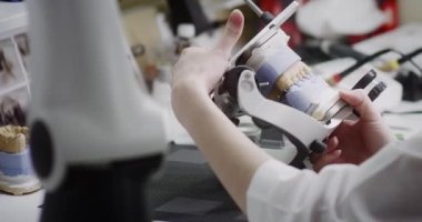 Bir diş teknisyeni elinde çene eklem makinesinin maketini tutuyor..