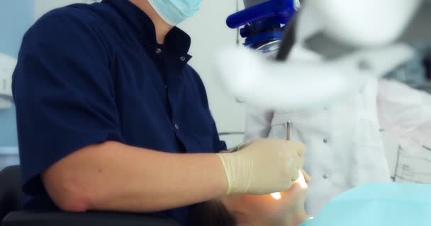 Un dentista e un assistente in maschera e guanti effettuano la pulizia professionale dei denti al microscopio a un paziente in un moderno studio dentistico. — Video Stock