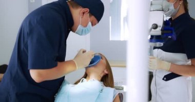 Erkek bir dişçi hastaya bir cofferdam çıkarmak için bir prosedür uygular..