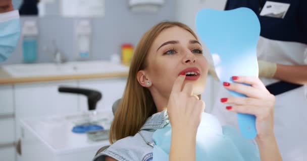 O femeie frumoasă își arată dinții în oglindă dentistului. — Videoclip de stoc