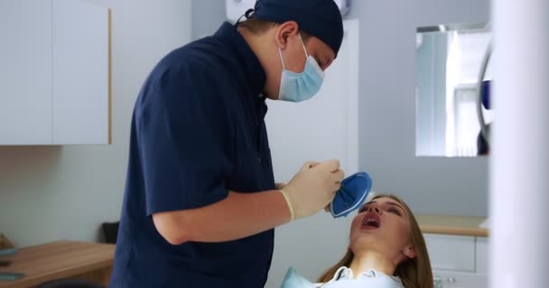 Un dentist de sex masculin efectuează procedura de aplicare a unui cafferdam la pacient. — Videoclip de stoc