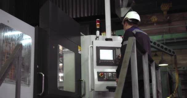 Um trabalhador profissional em um capacete fica atrás de uma máquina CNC. — Vídeo de Stock