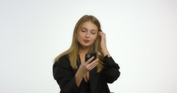 Vacker kvinna med långt blont hår i svart jacka ringer ett telefonnummer — Stockvideo