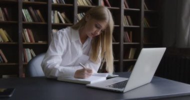 İş kadını laptopun önünde düşünceli bir şekilde notlar yazıyor..