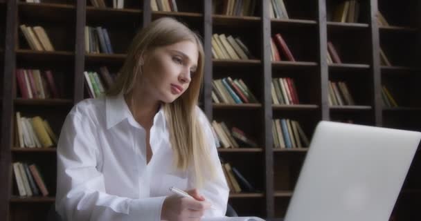Beyaz gömlekli bir iş kadını dizüstü bilgisayarda çalışır ve notlar alır.. 