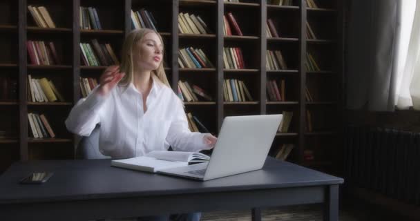 Liikenainen valkoisessa paidassa työskentelee kannettavassa tietokoneessa ja tekee muistiinpanoja. — kuvapankkivideo