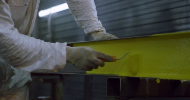 Trabajo industrial: Hombre en overoles pinta estructuras metálicas con un rodillo amarillo — Vídeo de stock