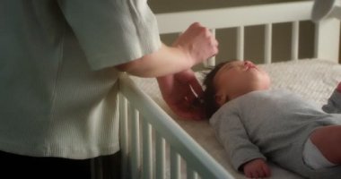 Sevgi dolu anne, yeni doğmuş bir bebeği bebek beşiğinde sırtüstü yatarak tarıyor.. 