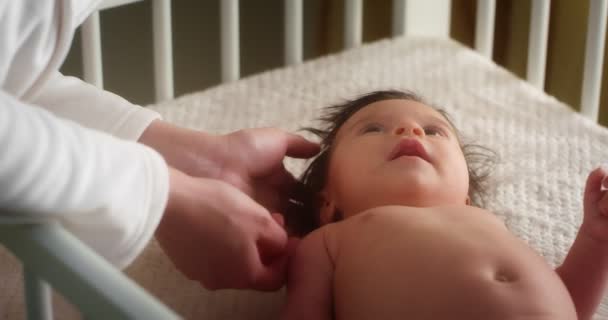 Турботлива мати погладжує новонароджену дитину, що лежить на спині у дитячому ліжечку . — стокове відео