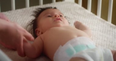 Bebek bezli bir bebeği beşiğinde sırt üstü okşayan şefkatli bir anne.. 