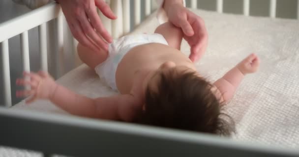 Zorgzame moeder strelen een pasgeboren baby in een luier liggend op haar rug in wieg. — Stockvideo