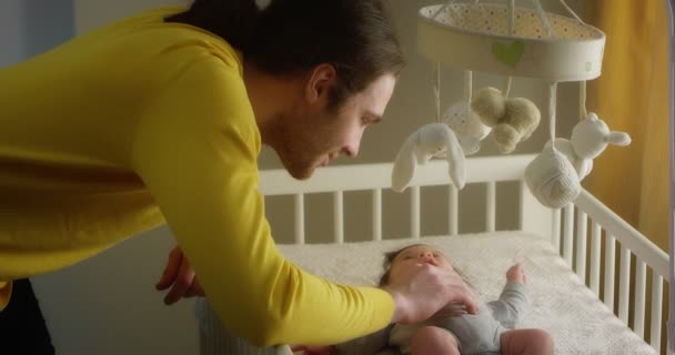Gelukkig jong vader streelt pasgeboren baby liggend in een kind wieg. — Stockvideo
