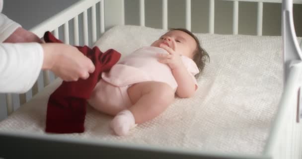 Заботливая мать одевает новорожденную девочку, лежащую на спине в детской кроватке. — стоковое видео