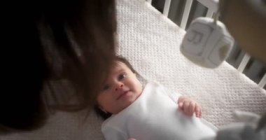 Bakıcı anne, yeni doğmuş bir bebeği beşiğinde sırt üstü yatarken okşar..