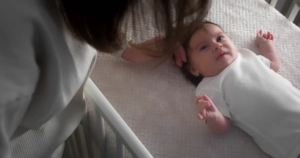 Любляча мама гладить новонароджену дитину, що лежить на спині у дитячому ліжечку . — стокове відео
