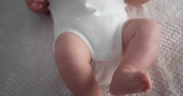 Newborn baby in a white bodysuit is lying on his back in a light child crib. — 图库视频影像