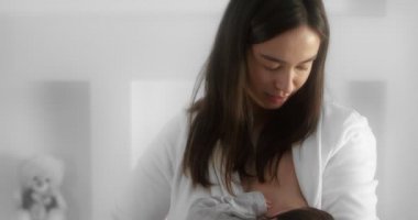 Mother is breastfeeding her newborn baby in the nursery. Mom cradles a infant.
