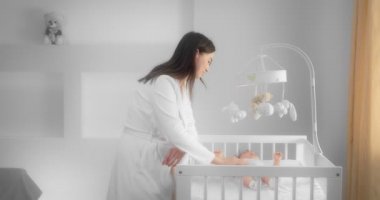 Mother in a white coat picks up a newborn baby lying in a child crib. 